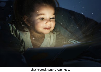 Cute Little Child Reading Magic Book In Darkness