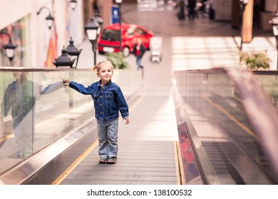 Cute little child in shopping center standing on moving staircase, escalator