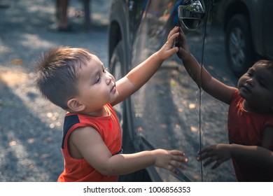 Cute Little Child Touching A Black Car Reaching For Car Door Handle With Reflection In Shining Black Car Door