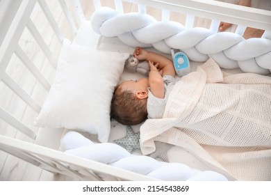 Niño pequeño con juguete y monitor para bebés durmiendo en cuna