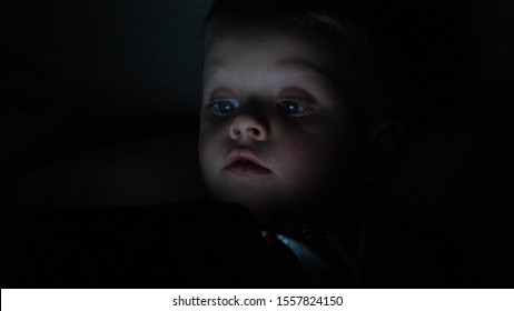 Cute Little Child Watching Cartoon On Smartphone In The Dark Room. Dangers Of Blue Light Damage His Eyes. Handsome Little Boy Can Get Age Related Macular Degeneration Of Blue Light.