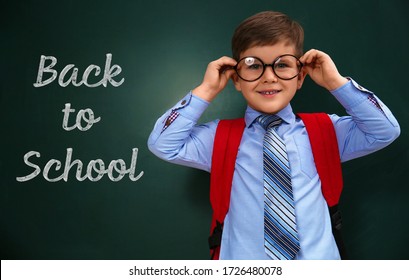 Cute Little Child Wearing Glasses Near Chalkboard With Phrase BACK TO SCHOOL