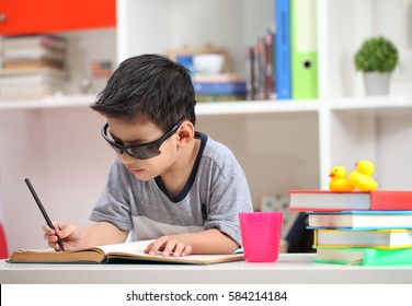 Cute Little Child Wearing Sunglasses And Doing Homework Reading A Book Coloring Pages Writing And Painting. Preschoolers Learn To Write And Read. Asian Boy Write And Read Homework In The Room.