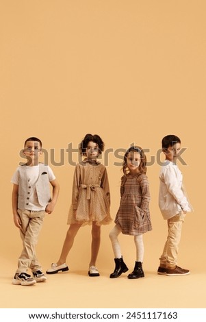 Cute little children, boys and girls dressed glamour outfits with trendy hairstyles posing against beige studio background. Concept of fashion and style, beauty, childhood, Black Friday, Cyber Monday.