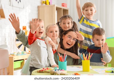 Cute little children hugging nursery teacher in kindergarten