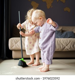 Cute little children infant boy and toddler girl in linen clothes sweeping floor in room with broom, helping mom with house chore at home. Baby boy brother and older sister spending time together