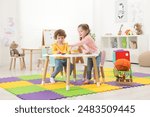 Cute little children playing with colorful toy pyramid at white table in kindergarten