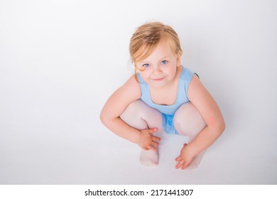 Cute Little Chubby Girl In A Blue Dance Leotard Sitting On White Background Looking Up From The Bottom.