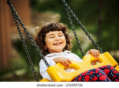 cute little curly girl riding on a swing, laughing