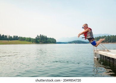 Cute little daring boy jumping off the boat dock at the lake. Being adventurous and brave, diving right into the water 
