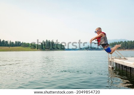 Cute little daring boy jumping off the boat dock at the lake. Being adventurous and brave, diving right into the water	
