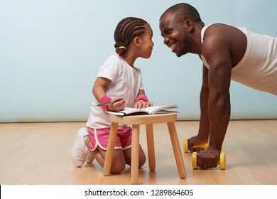 Cute Little Daughter Fitness Training Her Handsome Black Young Father. She Is Making Notes In Her Paper Notebook. Child Role Play. They Are Looking Into Each Other's Eyes, Giggling, Having Fun.