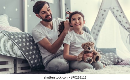 Cute little daughter and her handsome young dad are playing together in child's room. Dad is doing his daughter hair - Powered by Shutterstock