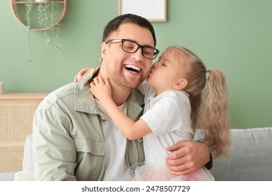 Cute little daughter kissing her happy father at home