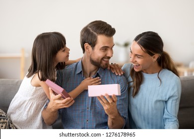 Cute Little Daughter And Loving Wife Making Funny Pleasant Surprise Congratulating Happy Husband Daddy Opening Gift Box, Excited Dad Holding Present From Family Celebrating Birthday Or Fathers Day