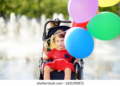 Cute little disabled girl in a wheelchair celebrate birthday or walking in the Park summer. Child cerebral palsy. Inclusion. Family with disabled kid.
