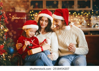 Cute little festive girl openng xmas gifts on Christmas eve with mom and dad, decorated kitchen interior, copy space - Powered by Shutterstock