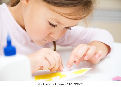 Cute little girl applying a color paper using glue while doing arts and crafts in preschool