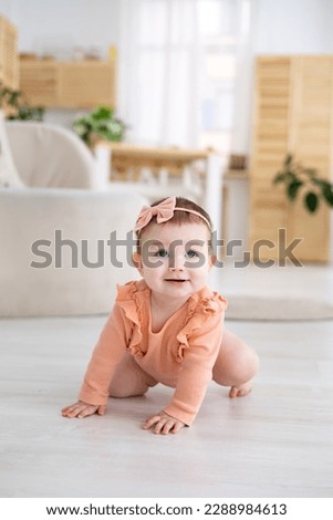 a cute little girl baby in a pink bodysuit crawls in the bright living room of the house, the baby's first steps, the baby is learning to walk