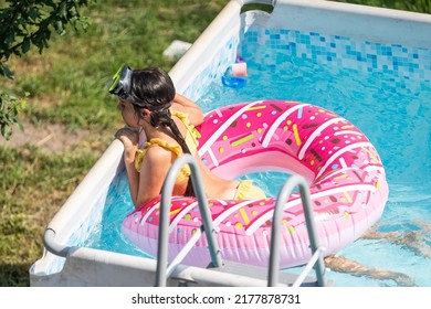Cute little girl in a bathing suit lying on a donut inflatable circle. The child swims on a blue background