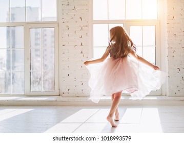 Cute little girl in beautiful dress is dancing at light sunny room