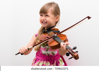 Cute little girl in a beautiful dress playing violin. Joyful and happy emotions. Training. Education. School. Aesthetic training. Elementary classroom. - Powered by Shutterstock