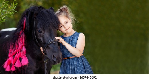 Cute little girl and black pony in a beautiful park. Pretty girl embracing  a pony. Spring or summer time. Copy space for text. Banner