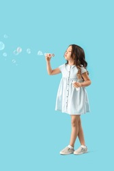 Cute Little Girl Blowing Soap Bubbles On Light Blue Background