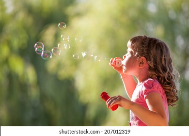 Cute little girl with blowing soap bubbles in park