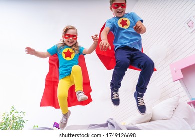 cute little girl and boy jumping from bed to fly, play superhero with cloak and mask at home in kids bedroom. The concept of defenders and saviors in the face of a small child. leap of faith