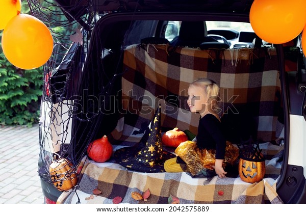 Cute little girl celebrating Halloween in car\
trunk. Stay home celebration. Autumn holidays. Trick or treat.\
Halloween in isolation