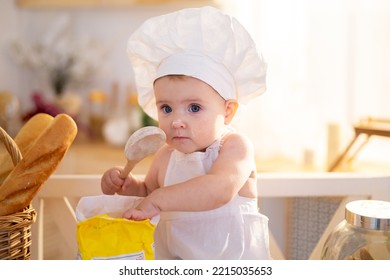 A Cute Little Girl In A Chef's Hat And An Apron Is Sitting On The Table In The Kitchen At Home With A Rolling Pin, Flour, Loaves Of Bread, A Little Cook, Homemade Food