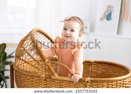 a cute little girl child in a pink bodysuit is standing in a wicker cradle at home, looking at the camera, smiling, children's healthy sleep