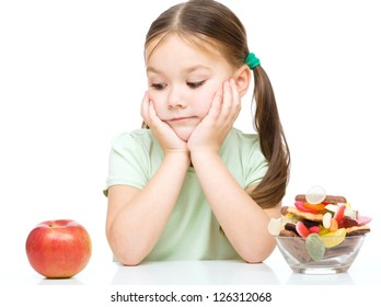 Cute kleine Mädchen, die zwischen Äpfeln und Süßigkeiten wählen, einzeln auf Weiß