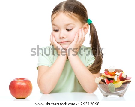 Cute little girl choosing between apples and sweets, isolated over white