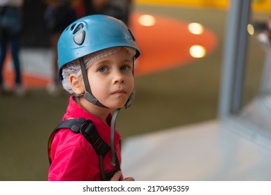 Cute little girl climber in blue protective helmet and gear for climbing standing in climber centre amusement park for children. Caucasian female climber 5 years