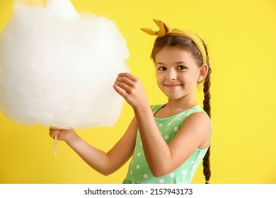 Cute little girl with cotton candy on yellow background