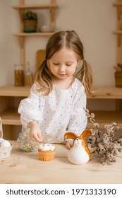 Cute little girl in a cotton dress at home in a wooden kitchen prepares an Easter cake