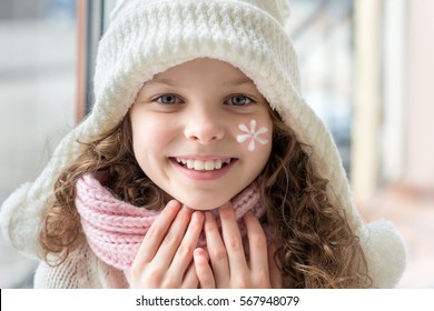 Cute Little Girl With Cream On Her Face. Skin Protection From Cold. Seasonal Concept.  Portrait Of Smiling Kid In Winter Clothes.