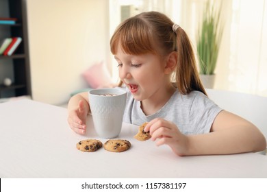 Cute little girl with cup of hot cocoa drink and cookies at home