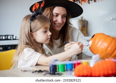 Cute little girl daughter holding paintbrush while painting Halloween pumpkins together at home