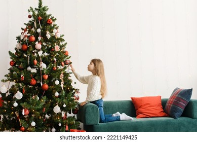 A cute little girl decorates the Christmas tree on Christmas morning.