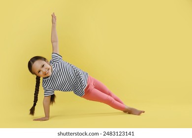 Cute little girl doing gymnastic exercise on yellow background, space for text - Powered by Shutterstock