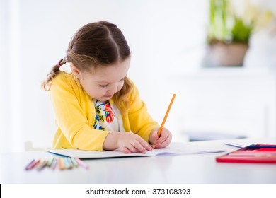 Cute Little Girl Doing Homework, Reading A Book, Coloring Pages, Writing And Painting. Children Paint. Kids Draw. Preschooler With Books At Home. Preschoolers Learn To Write And Read. Creative Toddler