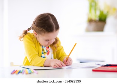 Cute Little Girl Doing Homework, Reading A Book, Coloring Pages, Writing And Painting. Children Paint. Kids Draw. Preschooler With Books At Home. Preschoolers Learn To Write And Read. Creative Toddler