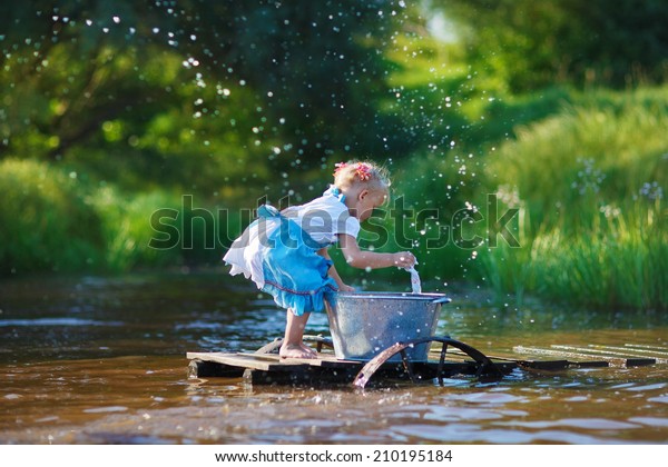 A cute little girl doing the laundry in a small\
aluminium basin standing on a pontoon at the pond in a sunny summer\
day. Kids are playing.