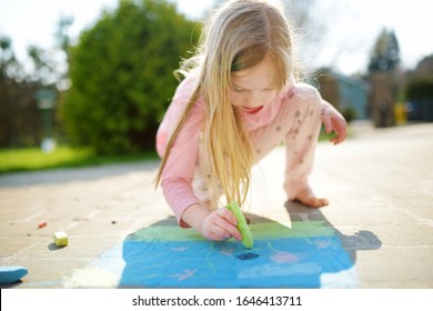 Cute Little Girl Drawing With Colorful Chalks On A Sidewalk. Summer Activity For Small Kids. Creative Leisure For Family.