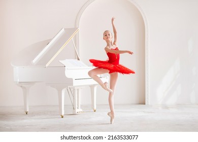cute little girl dreams of becoming professional ballerina. In a white room, next to a piano, girl in a bright red tutu is dancing on pointe shoes. Vocational school student.