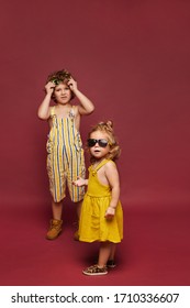 Cute little girl in a dress and sunglasses and little boy in a summer stylish overalls and sunglasses, isolated in full length at the pink background