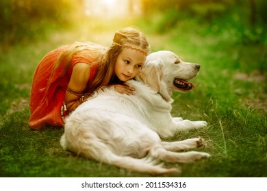 Cute little girl dressed in hippie style sits on the grass and hugs her beloved dog. Summertime. Kids and pets.